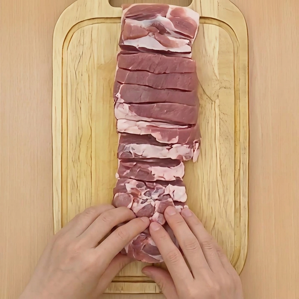 도마 위에서 양손으로 삼겹살 덩어리를 원통형으로 촘촘하게 마는 모습.