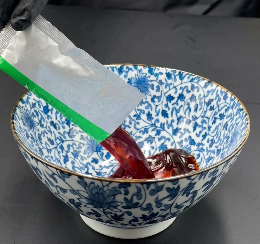 푸른 패턴의 도자기 그릇에 진한 간장 라멘 소스를 짜넣는 손.