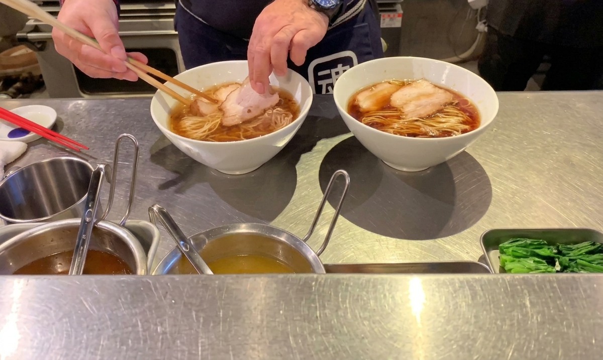 정리된 면 위에 젓가락으로 잘 익은 돼지고기 차슈 조각을 조심스럽게 올리는 모습.