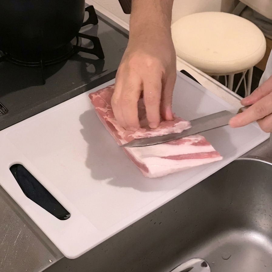하얀 도마 위에서 생삼겹살 안쪽에 칼집을 넣고 있는 모습