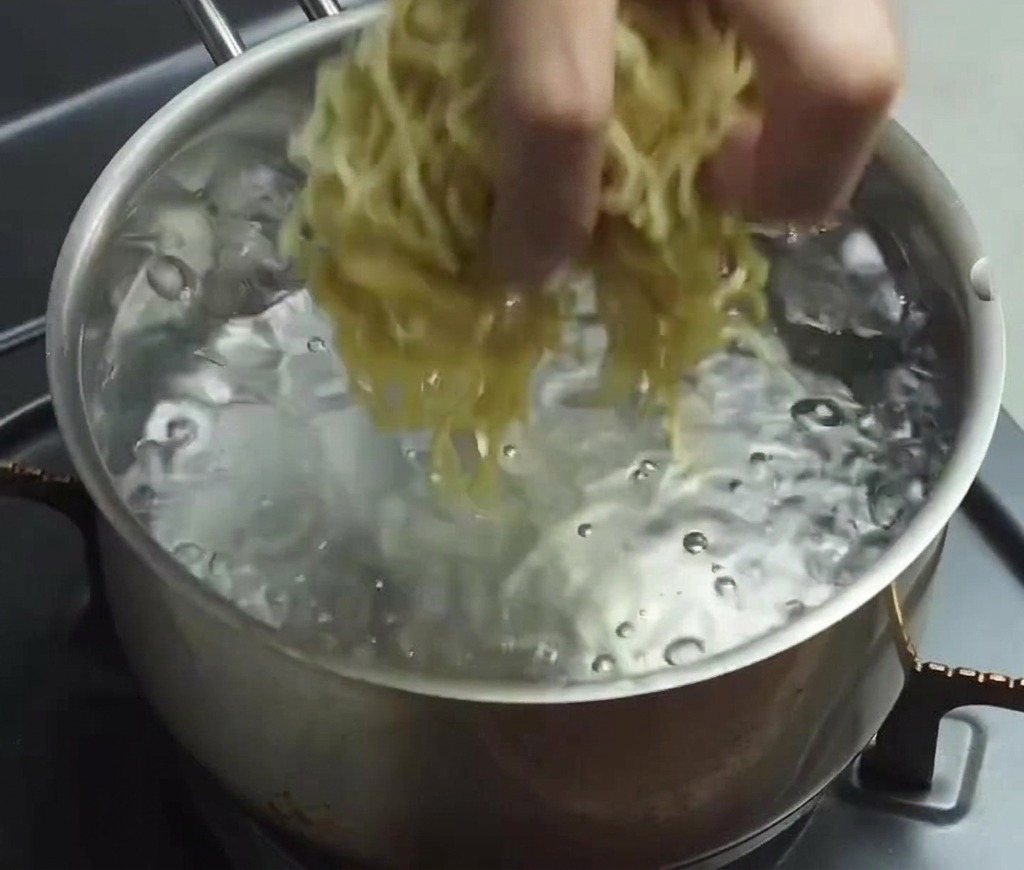 빠르게 끓는 맑은 물에 얇고 구불구불한 생라멘 면 뭉치를 넣는 손