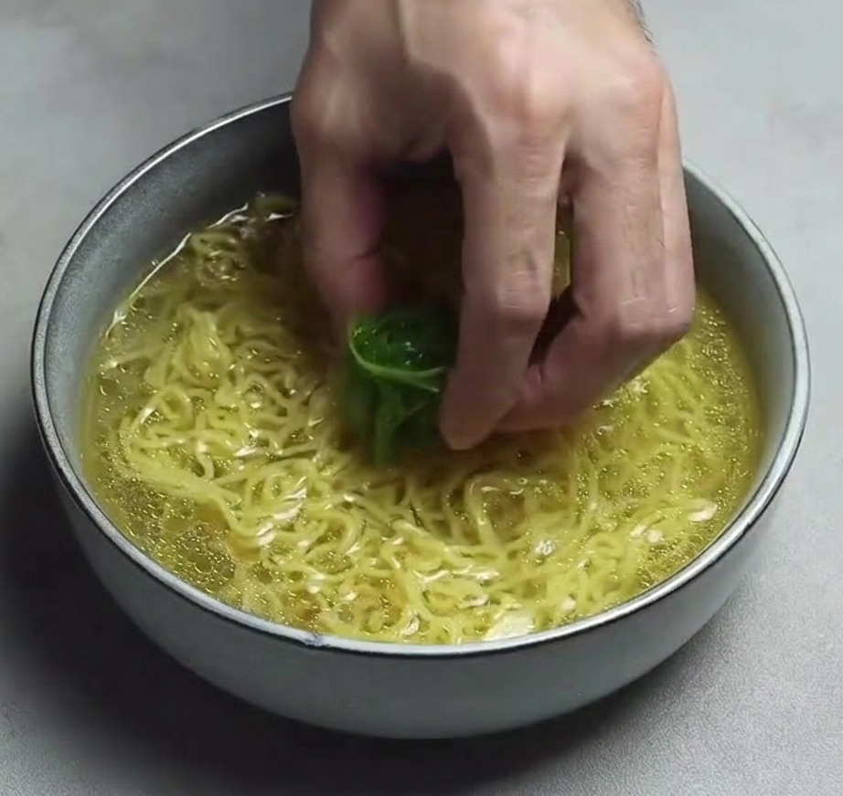 맑은 노란 육수가 담긴 라멘 면 위에 가늘게 채 썬 대파 한 줌을 올리는 손