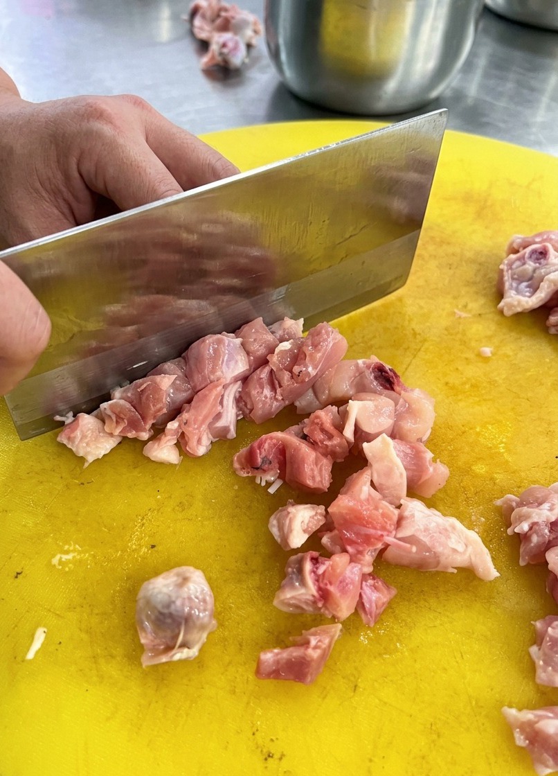 노란 플라스틱 도마 위에서 커다란 중식도로 생닭고기를 다지고 있는 모습.