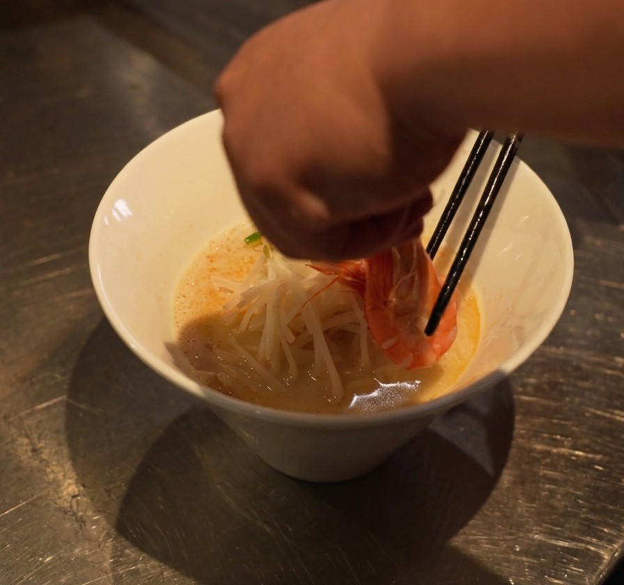 젓가락으로 익힌 새우를 그릇의 면과 숙주 위에 정성스럽게 올리는 모습.