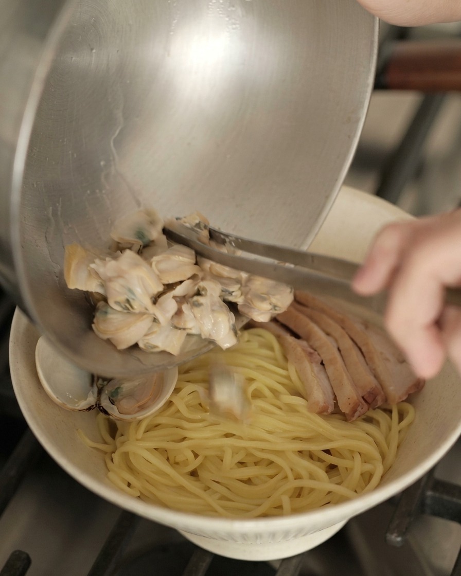 완성된 라멘 그릇 위에 미리 익혀둔 바지락들을 그릇째 쏟아 올리는 모습.
