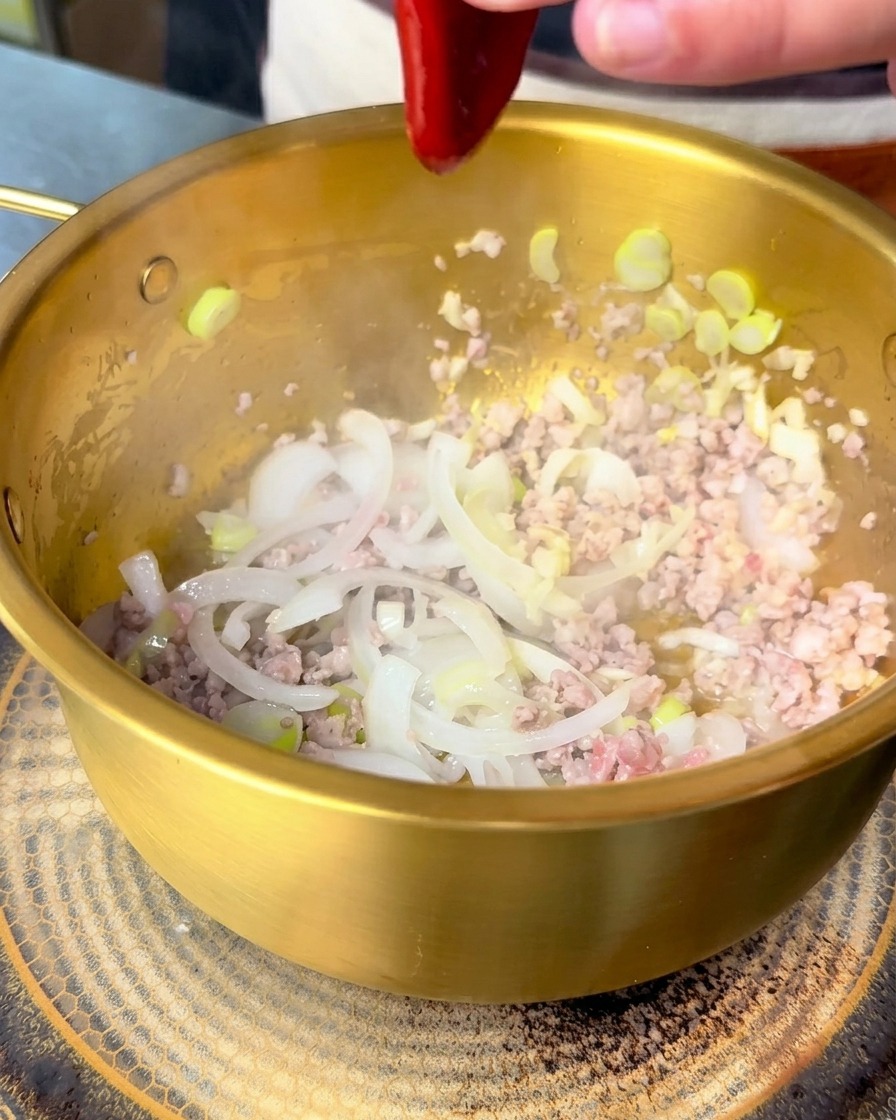 볶은 고기와 양파 위에 빨간 비빔장을 짜 넣는 모습.
