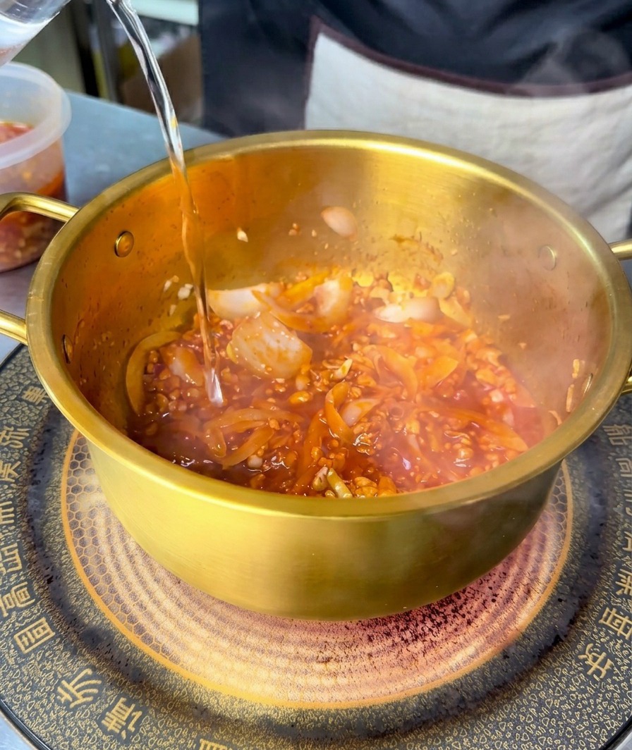 빨갛게 볶아진 재료 위에 맑은 물을 붓는 모습.