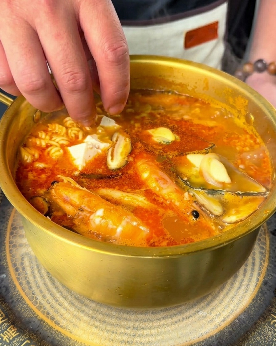 끓는 라면에 순두부 조각과 고추 고명을 넣는 모습.