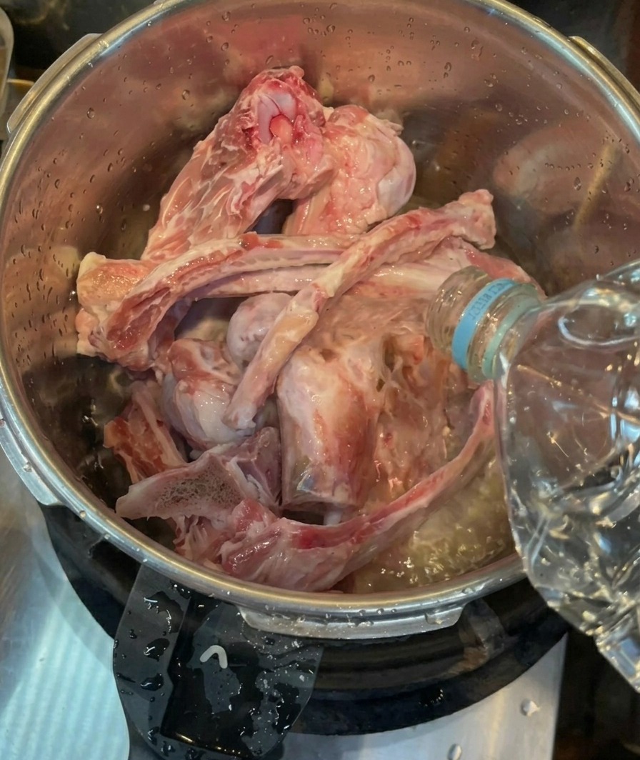 스테인리스 압력솥에 담긴 손질된 돼지뼈 위로 생수를 붓는 모습