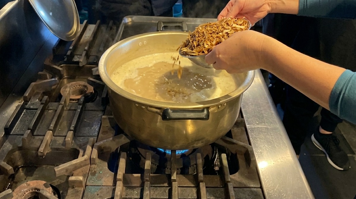 보글보글 끓고 있는 진한 우윳빛 육수 냄비에 말린 멸치를 한 가득 넣고 있는 모습.