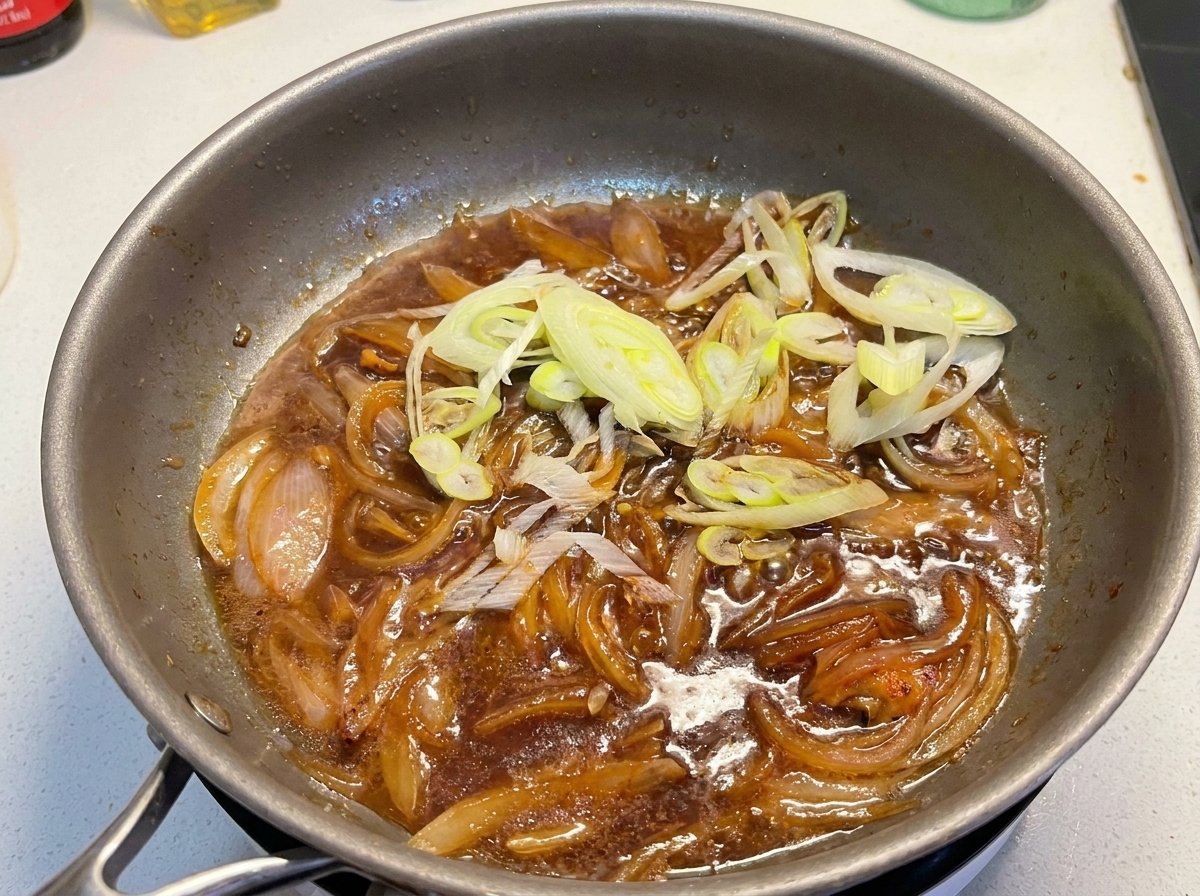 보글보글 끓는 소스와 익은 양파가 담긴 팬에 썬 쪽파를 넣는 모습.
