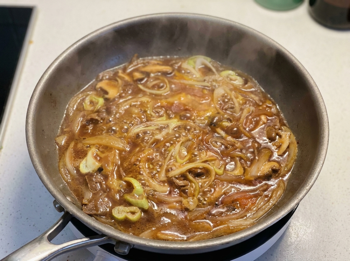 보글보글 끓는 소스와 쪽파, 양파가 있는 팬에 푼 달걀을 부드럽게 두르는 모습.
