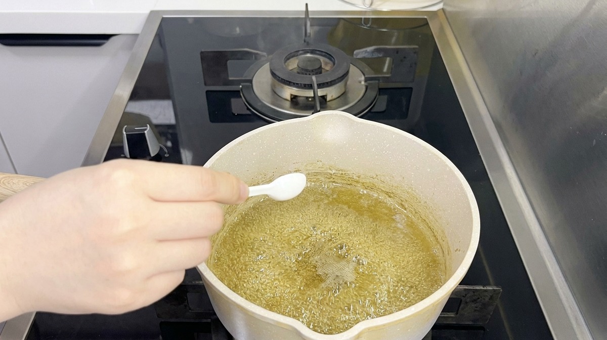 하얀 작은 스푼으로 냄비 속 끓고 있는 연둣빛 국물에 양념을 더하는 모습