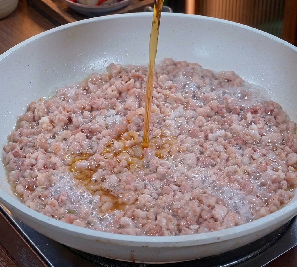 볶고 있는 다진 돼지고기에 투명한 호박색 맛술을 붓는 모습
