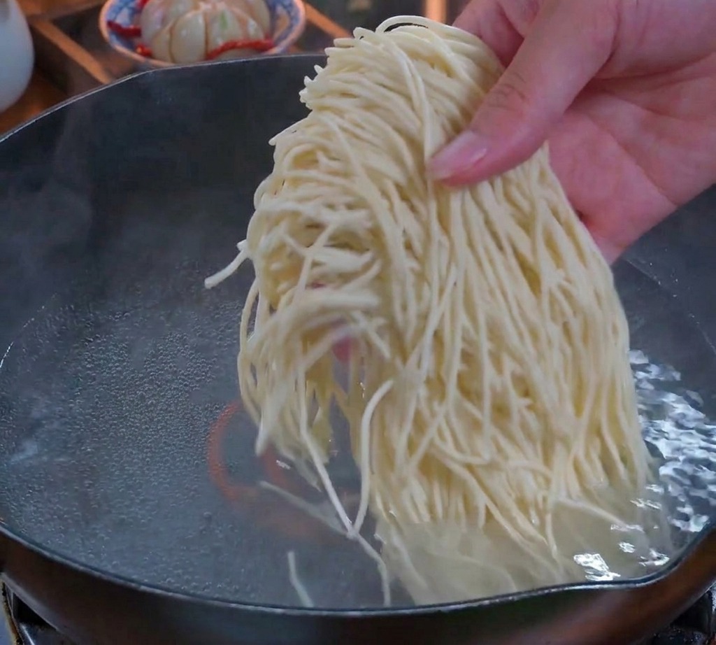 펄펄 끓는 물이 담긴 냄비에 얇은 생면 한 줌을 넣는 모습