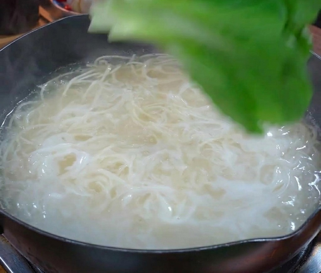 하얀 면이 끓고 있는 냄비에 신선한 푸른 잎채소를 넣는 모습
