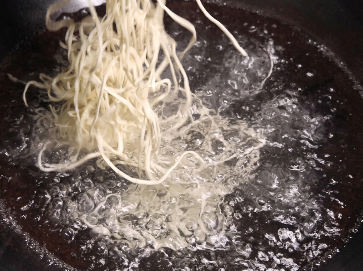 격렬하게 끓어오르는 냄비의 물속으로 하얗고 신선한 생면 한 묶음을 넣는 모습.