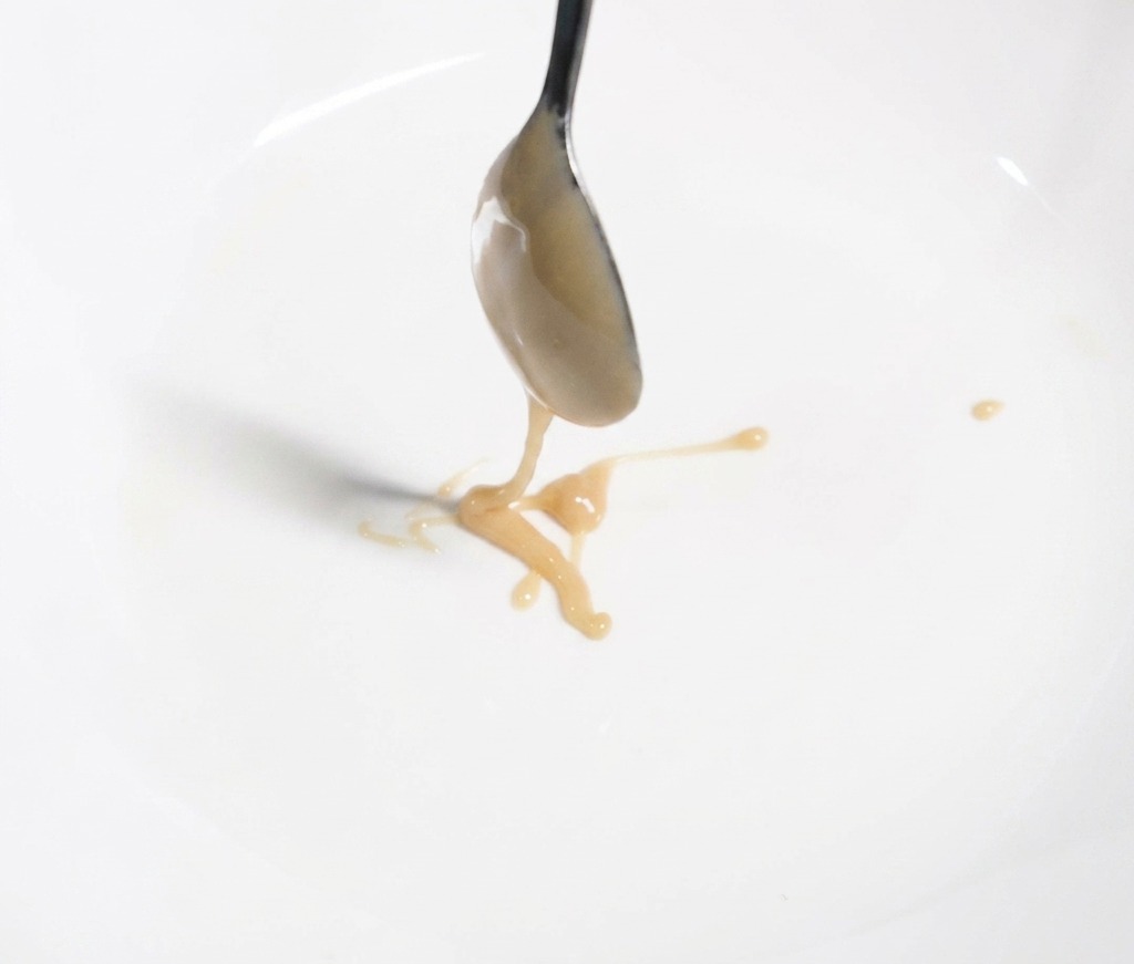 하얀 대접에 걸쭉하고 연한 갈색의 지마장을 쇠숟가락으로 덜어 담으며 면 소스 베이스를 만드는 모습.