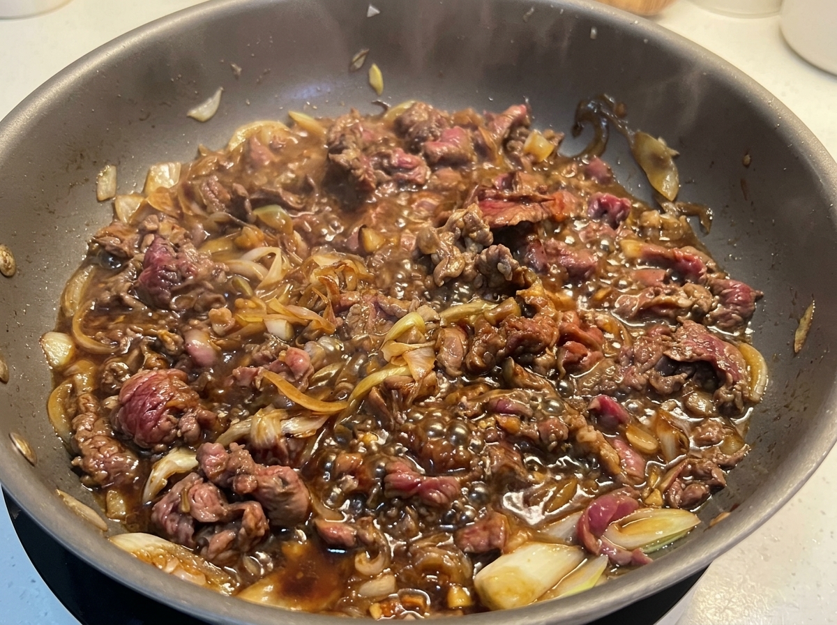 갈색으로 맛있게 익은 얇은 소고기가 양파와 함께 자작하고 진한 간장 소스에서 보글보글 졸여지는 모습.