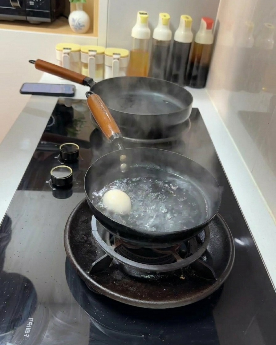 가스레인지 위 팔팔 끓는 물이 담긴 작은 냄비에 하얀 달걀 하나가 잠겨 있는 모습.