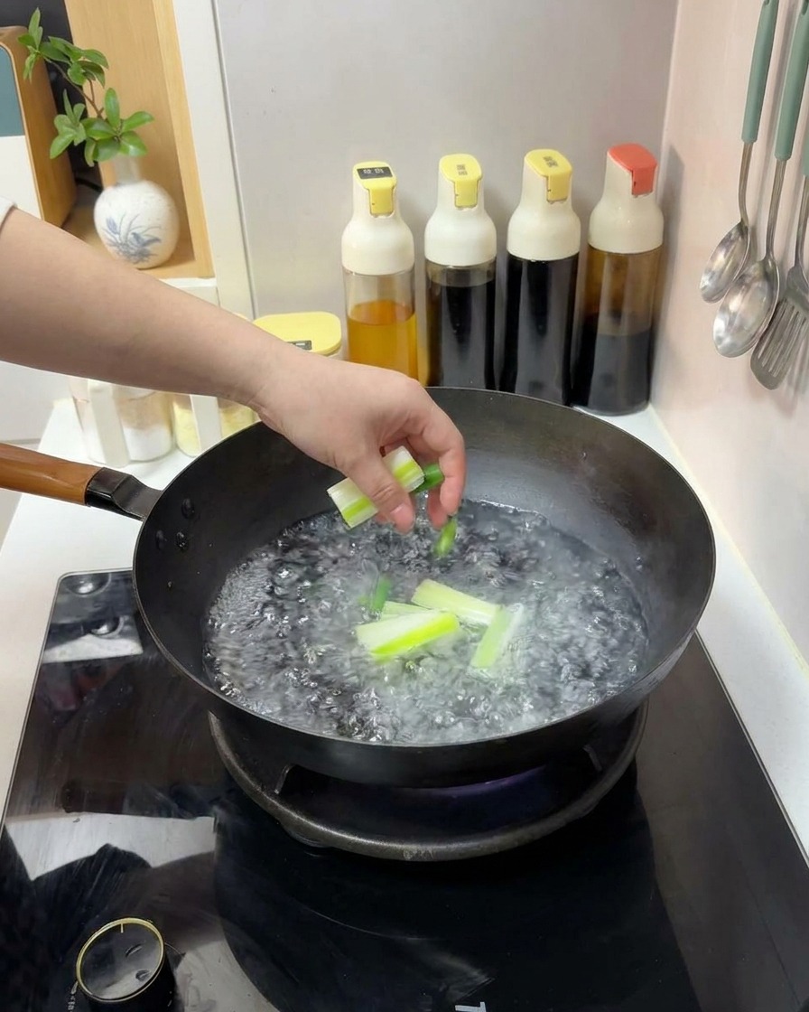 손으로 끓는 물이 담긴 웍에 큼직하게 썬 대파를 넣는 모습.