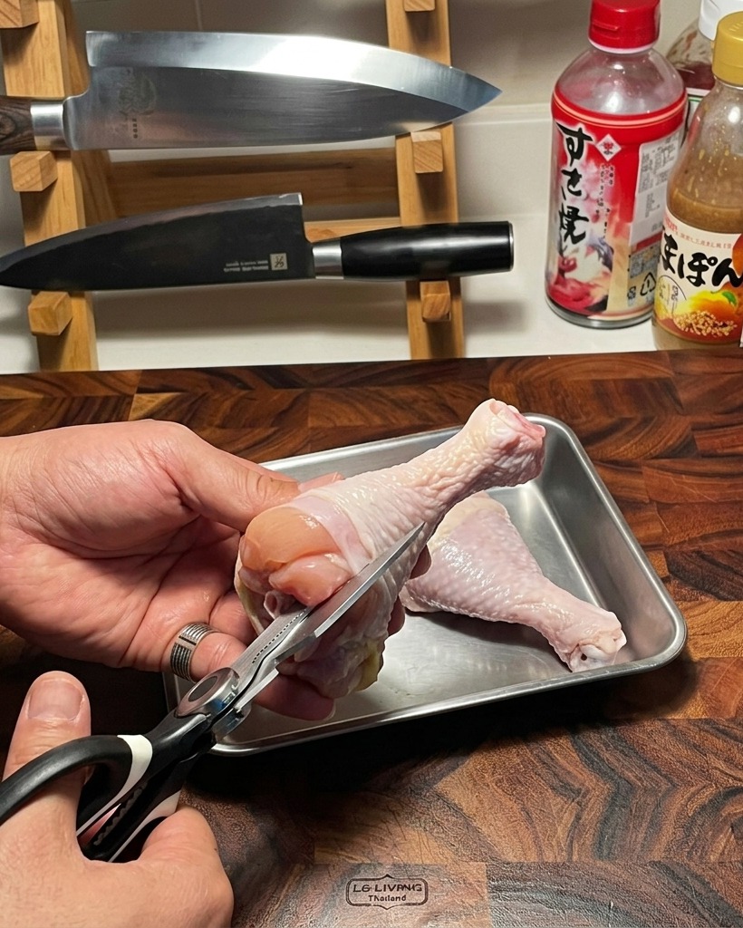 나무 도마 위에서 주방 가위로 신선한 생 닭다리살의 뼈를 조심스럽게 발라내는 모습.