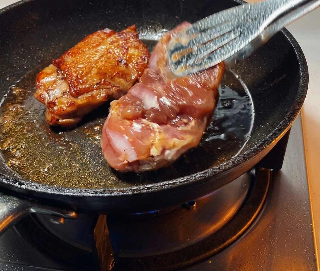 집게를 이용해 프라이팬 속의 닭다리살을 뒤집자 완벽하게 노릇하고 바삭해진 껍질이 드러나는 모습.