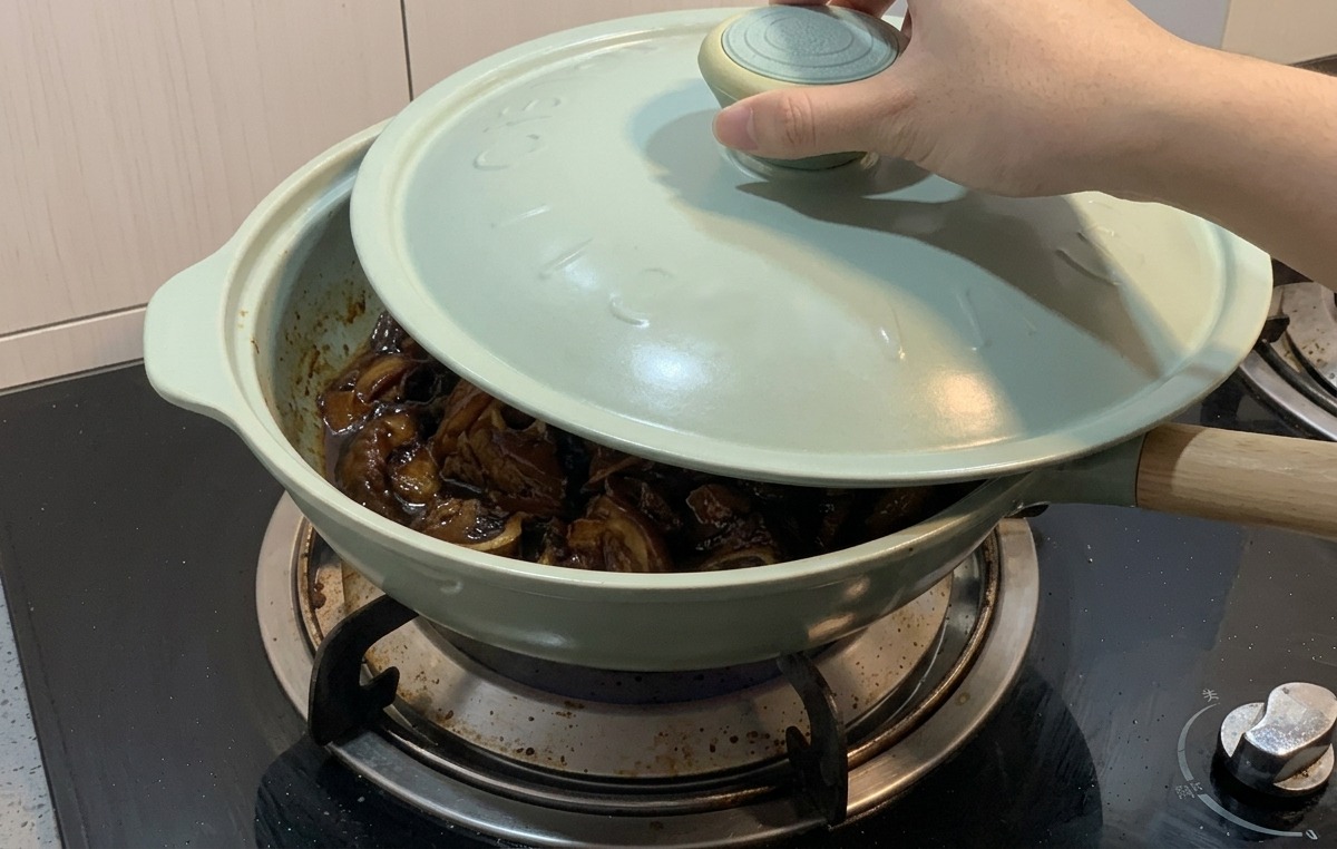 닭고기와 양파가 짙은 소스에 자작하게 끓고 있는 연두색 프라이팬 위로 손이 하늘색 뚜껑을 덮고 있는 모습.