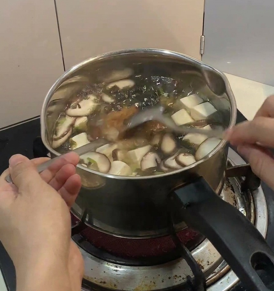 나무 테이블 위 모락모락 김이 나는 닭고기 달걀 덮밥 위에 손으로 송송 썬 쪽파와 가느다란 김 가루를 정성스럽게 뿌리는 모습.