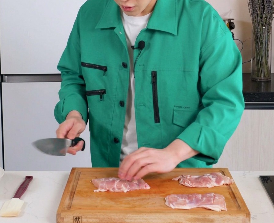 나무 도마 위에서 칼로 순살 닭다리살의 살코기 부분에 얇게 칼집을 내는 모습.
