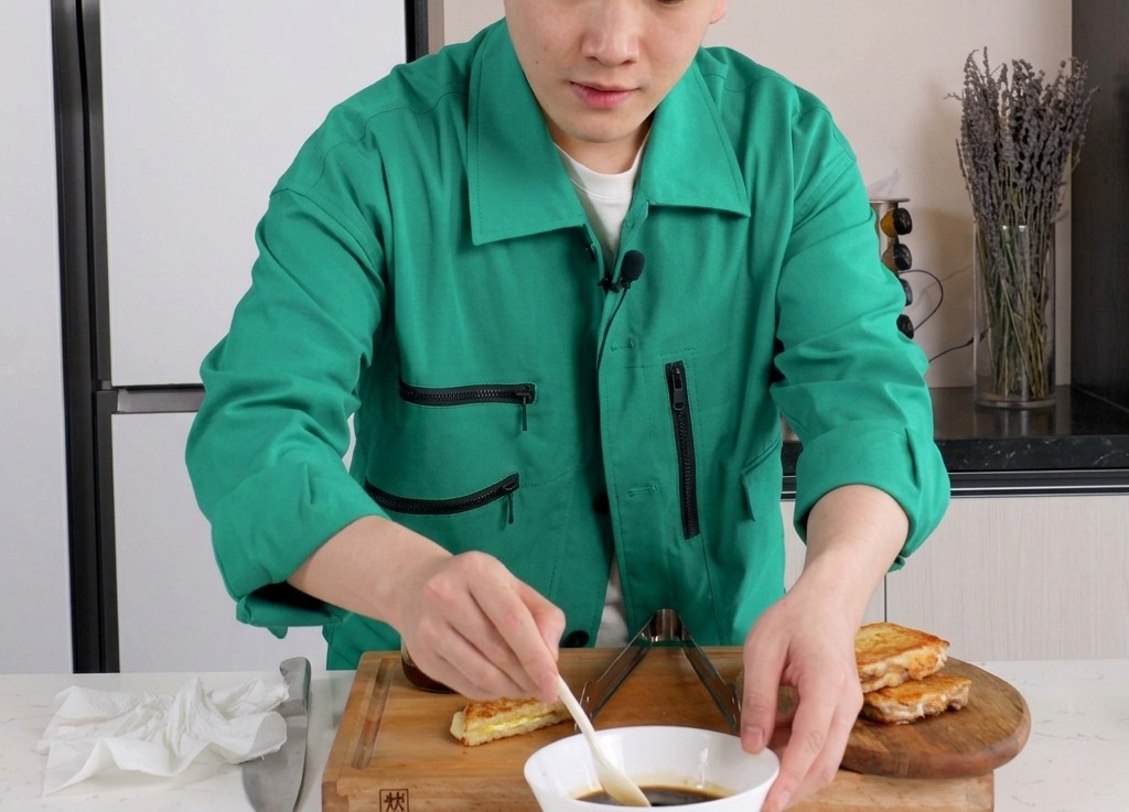 흰색 세라믹 볼에 담긴 진한 갈색 간장 소스를 작은 흰색 스푼으로 젓고 있는 모습.