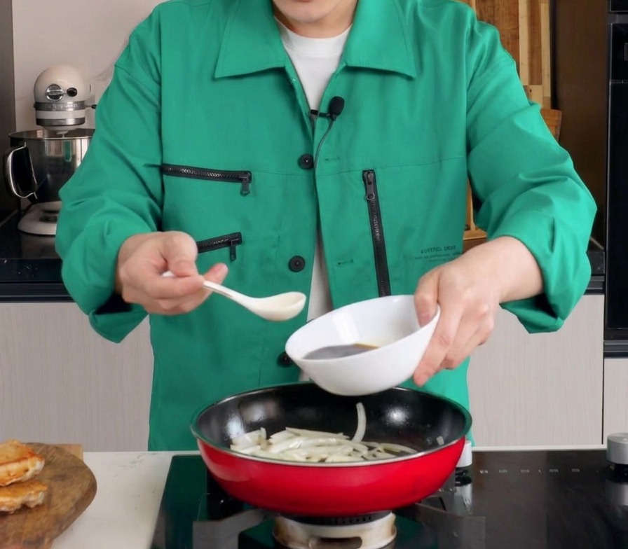 부드럽게 볶아진 양파가 담긴 붉은색 프라이팬에 흰 볼에서 진한 양념 소스를 붓는 모습.
