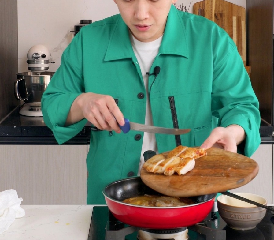 양파와 살짝 익은 달걀물이 있는 붉은색 팬에 썬 닭다리살을 올리는 모습.