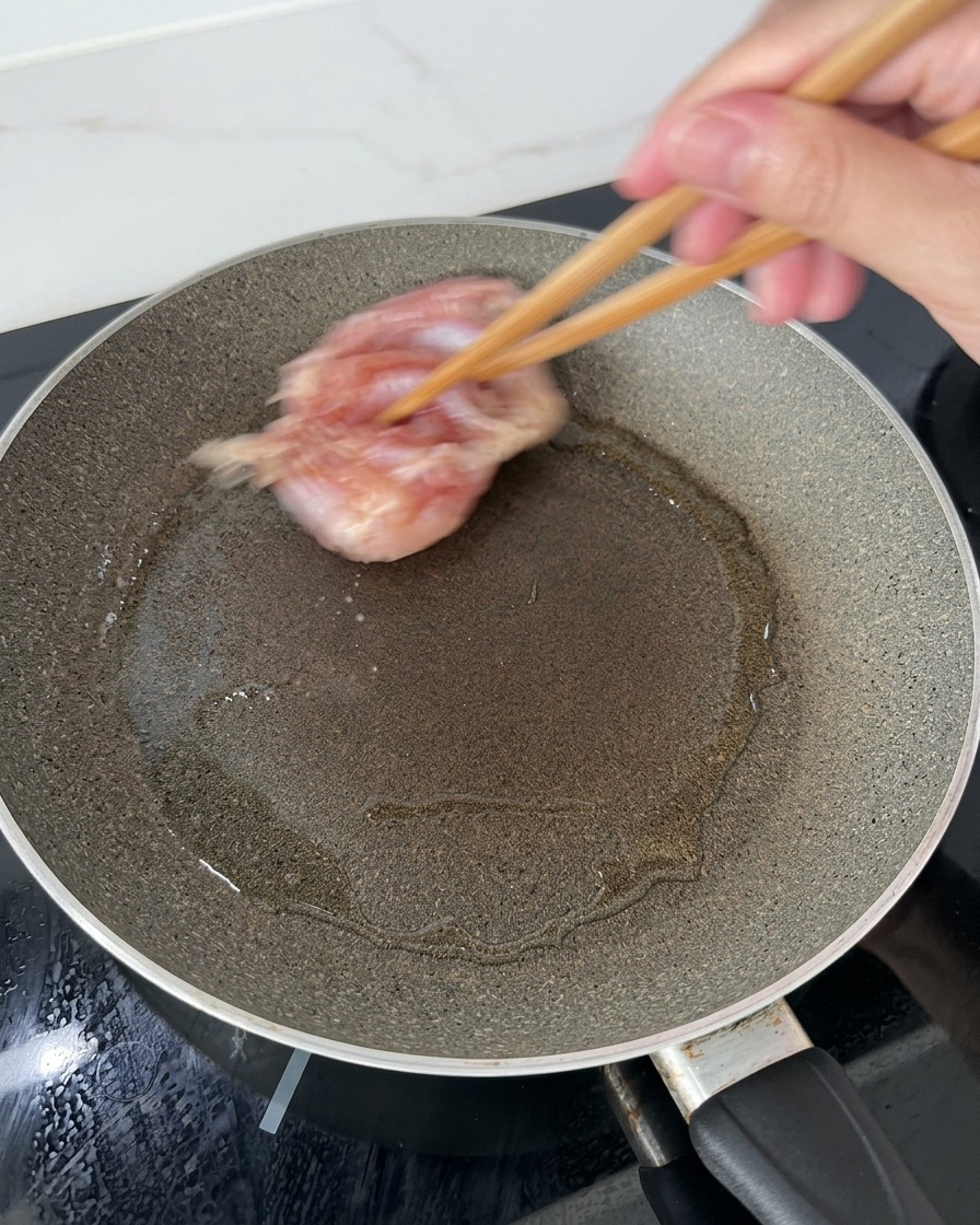 달구어진 기름진 프라이팬에 나무 젓가락을 이용해 밑간한 닭다리살의 껍질이 아래로 가도록 올리는 모습
