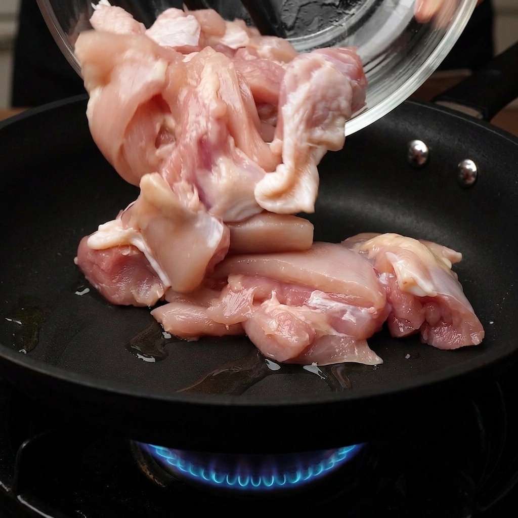 파란 가스 불 위의 달구어진 프라이팬에 유리 볼에 담긴 닭고기 조각들을 조심스럽게 넣는 모습