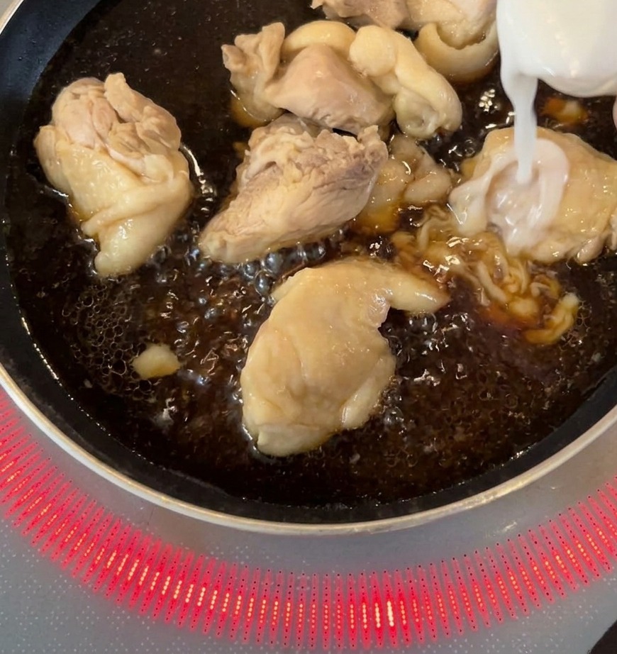 진한 소스에 졸여지고 있는 닭고기가 담긴 팬에 채 썬 양파를 넣는 모습.