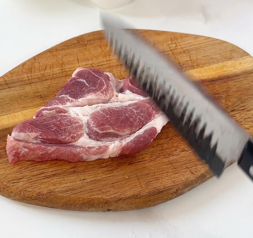 도마 위에서 무거운 칼등으로 돼지고기를 두드려 연육하는 모습