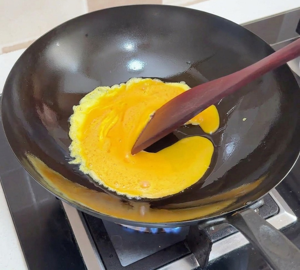 검은색 웍에서 익어가는 달걀을 주걱으로 가운데로 밀며 부드러운 결을 만드는 모습
