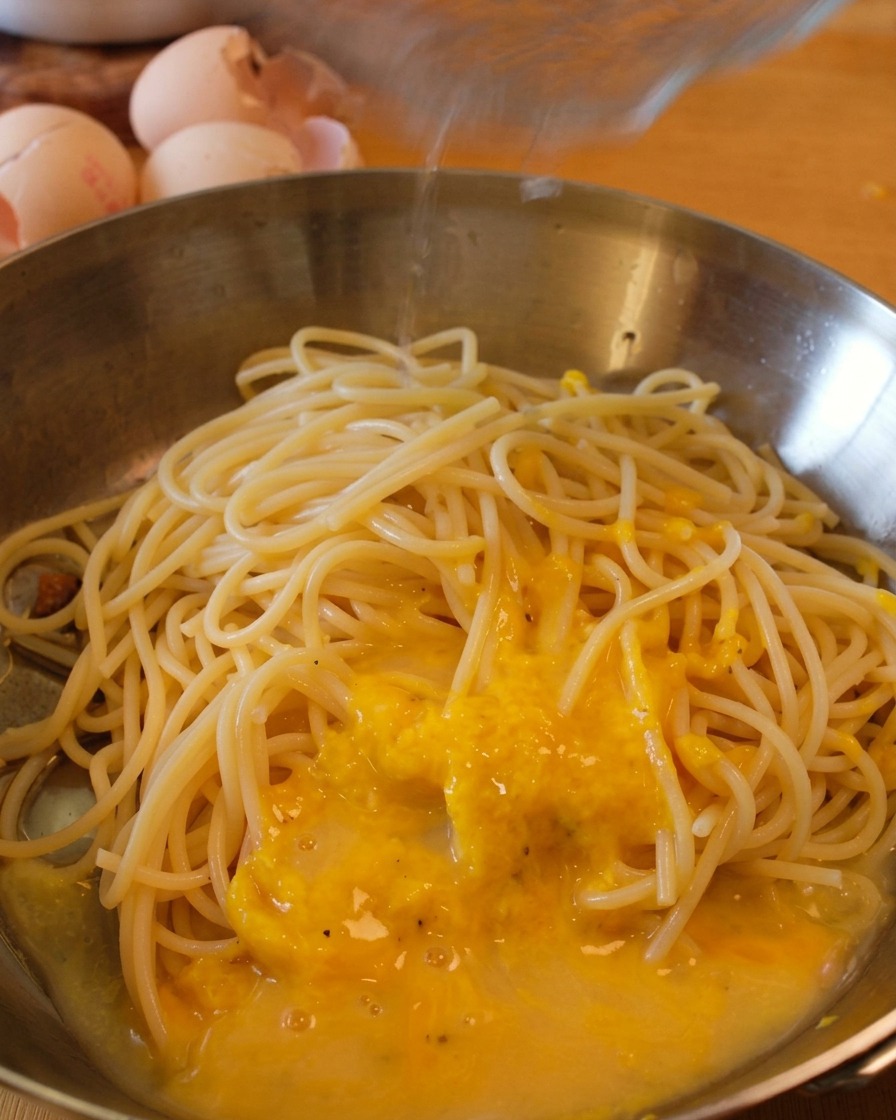 팬에 면수를 추가하며 노란 소스가 스파게티 가닥마다 코팅되도록 섞는 모습.