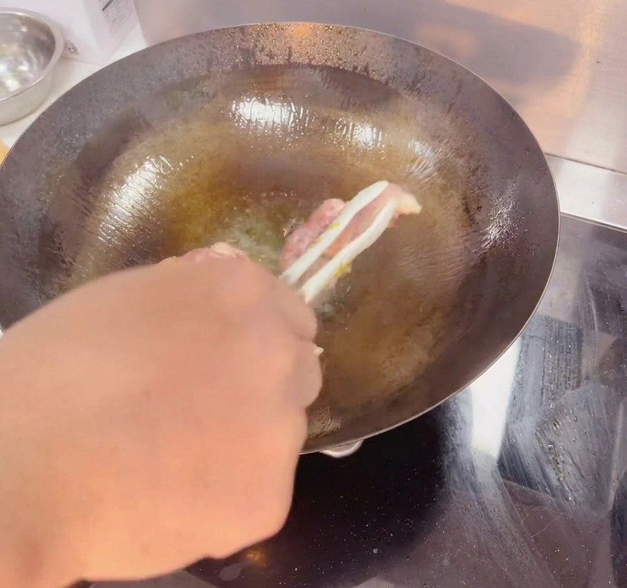 어두운 색 웍 안에서 요리용 집게로 닭다리살을 뒤집어 노릇노릇하고 바삭하게 구워진 껍질을 보여주는 모습.