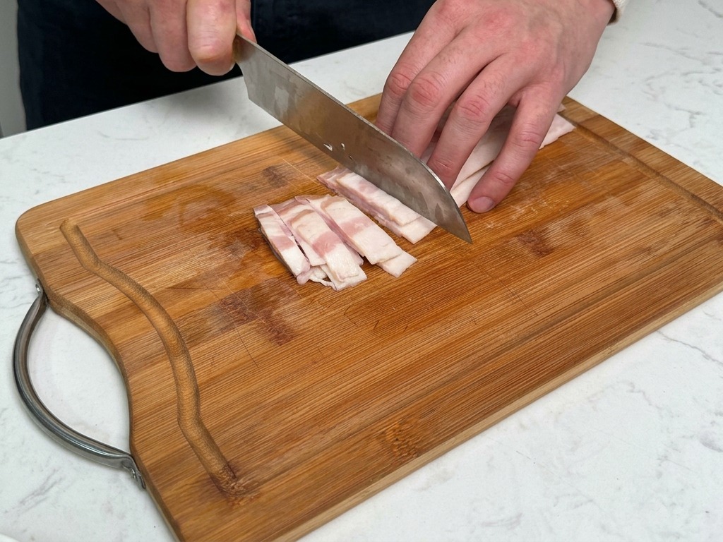 도마 위에서 두툼한 베이컨을 일정한 크기로 써는 모습