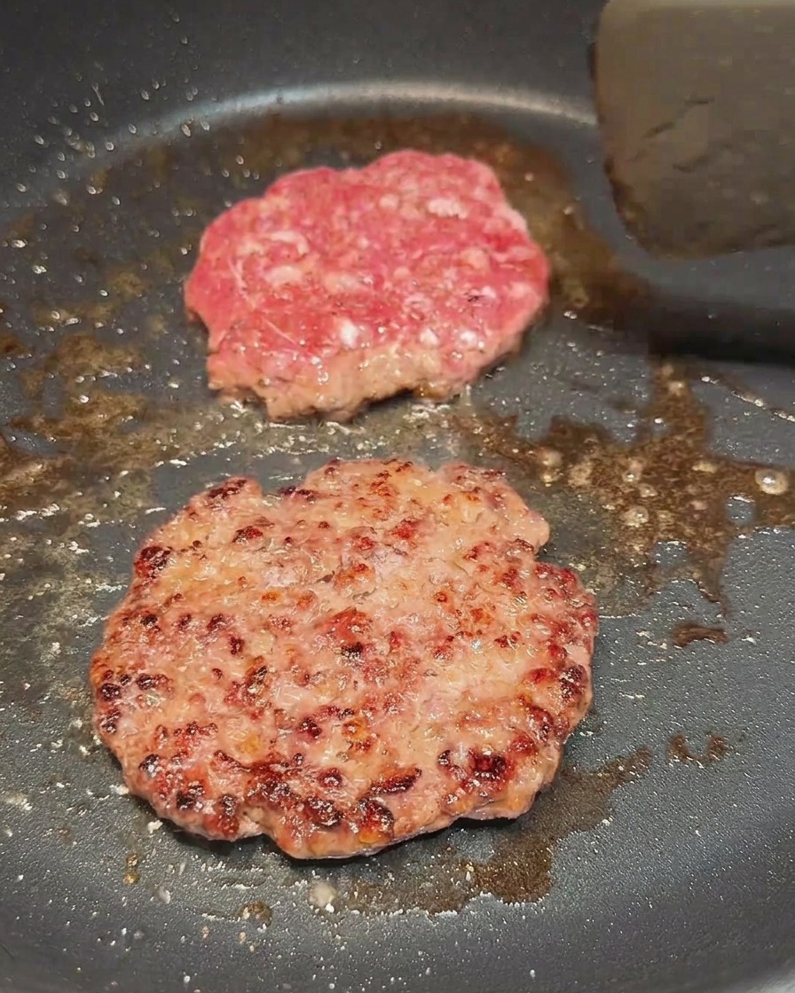 한쪽 면이 갈색으로 잘 익어 뒤집힌 소고기 패티의 모습.