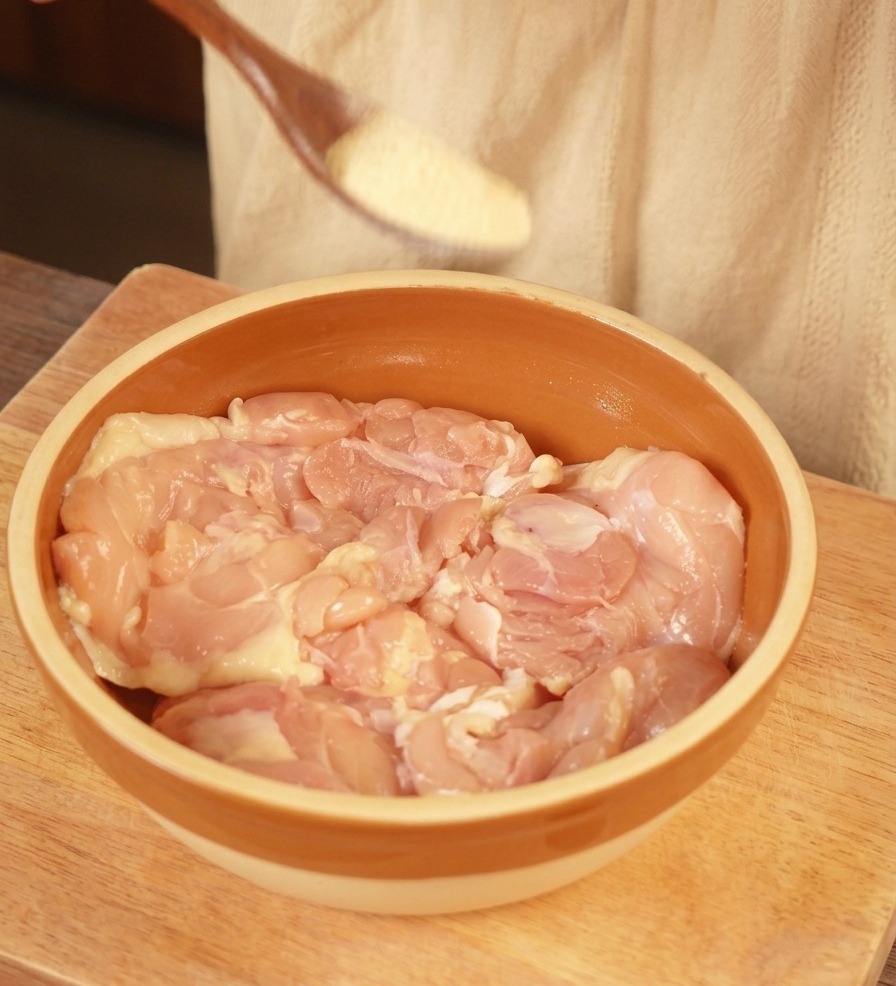 갈색 세라믹 볼에 담긴 뼈 없는 생 닭다리살 위에 마늘 가루를 뿌리는 모습