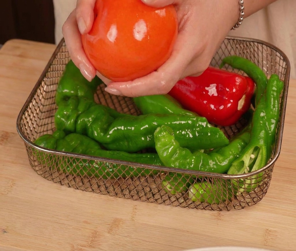 에어프라이어 바스켓 안에 기름을 바른 토마토와 고추들을 겹치지 않게 나란히 놓는 손