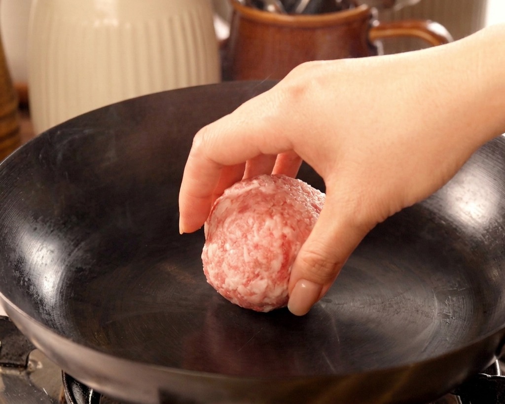 연기가 살짝 나는 뜨거운 무쇠 팬 위에 동그란 소고기 반죽을 올리는 손
