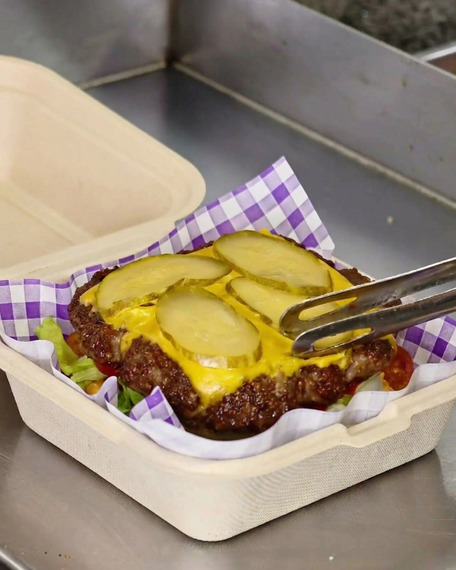 치즈와 피클이 올라간 패티를 토마토 위에 조심스럽게 옮기는 모습.