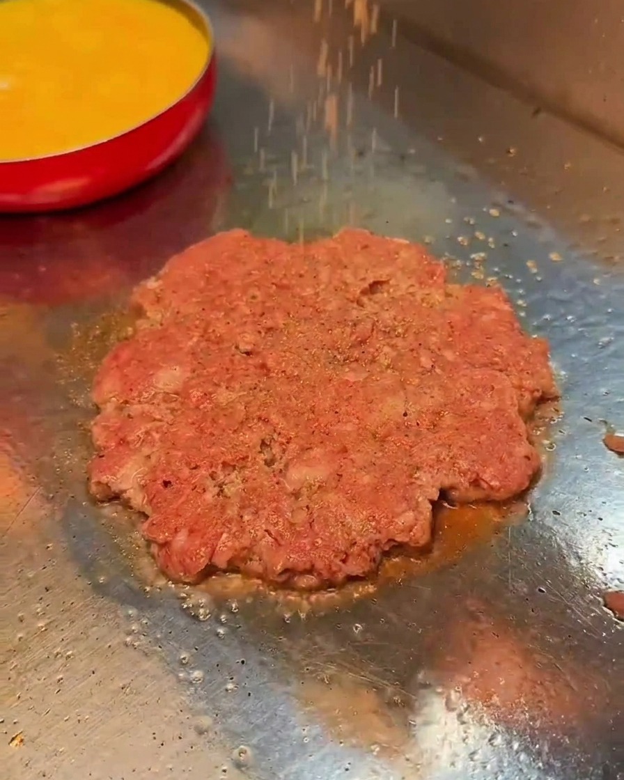 굽고 있는 소고기 패티 위에 소금과 후추를 뿌리는 장면.