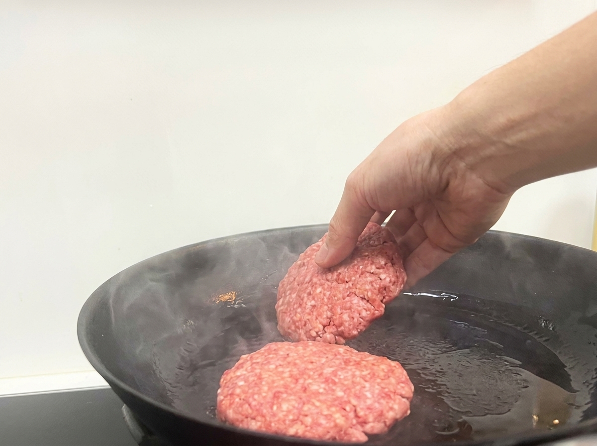 연기가 살짝 나는 뜨거운 팬에 소고기 패티 두 개를 올리는 모습
