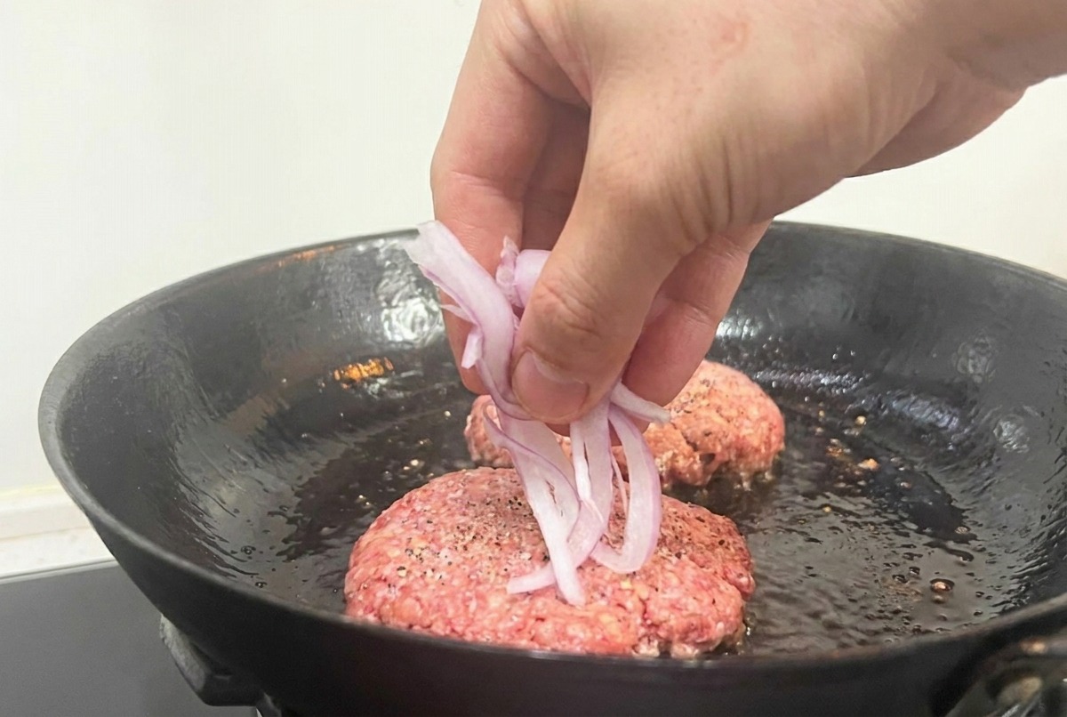 익지 않은 패티 윗면에 얇게 썬 적양파를 올리는 모습