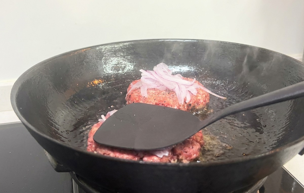 뒤집개로 양파가 올려진 패티를 꾹 눌러 평평하게 만드는 모습